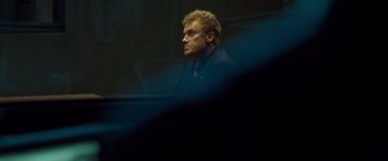 Movie still from “Salt” (2010), directed by Phillip Noyce – A man sitting at a table in a dark room; Close Up shot, Low angle