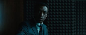 Movie still from “Salt” (2010), directed by Phillip Noyce – A man wearing a suit and tie in a dark room; Close Up shot, Over the shoulder angle