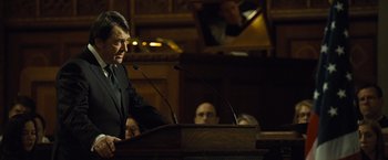 Movie still from “Salt” (2010), directed by Phillip Noyce – A man standing at a podium speaking to a crowd; Medium shot, Over the shoulder angle