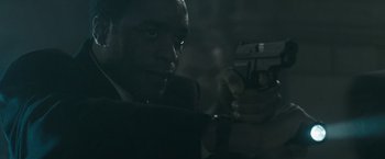 Movie still from “Salt” (2010), directed by Phillip Noyce – A man in a suit holding a gun in a dark room; Close Up shot, Over the shoulder angle