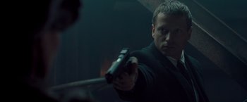 Movie still from “Salt” (2010), directed by Phillip Noyce – A man holding a gun while standing in a room; Close Up shot, Over the shoulder angle
