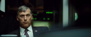 Movie still from “Salt” (2010), directed by Phillip Noyce – A man in a suit and tie sitting in front of a window; Close Up shot, Over the shoulder angle