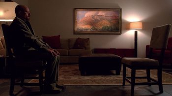 Movie still from “Breaking Bad” (2008), created by Vince Gilligan – A man sitting on a couch in front of a painting; Wide shot, Over the shoulder angle