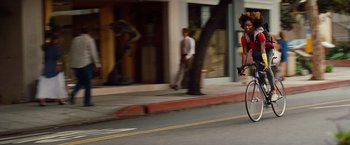 Movie still from “Savages” (2012), directed by Oliver Stone – A man riding a bike down a street past trees; Wide shot, Low angle