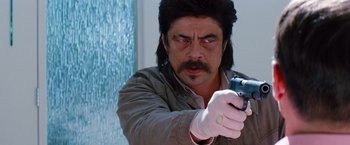 Movie still from “Savages” (2012), directed by Oliver Stone – A man in a brown jacket is holding a gun; Close Up shot, Over the shoulder angle