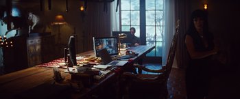Movie still from “Savages” (2012), directed by Oliver Stone – A man sitting in front of a computer on top of a table; Wide shot, High angle