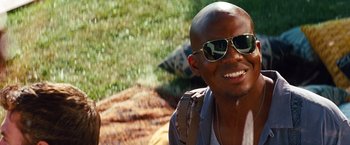 Movie still from “Savages” (2012), directed by Oliver Stone – A man wearing sunglasses and a backpack smiles for the camera; Close Up shot, Over the shoulder angle