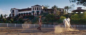 Movie still from “Savages” (2012), directed by Oliver Stone – A man in a cowboy hat is holding a lasso in front of a house; Wide shot, Low angle