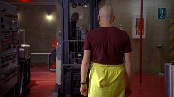 Movie still from “Breaking Bad” (2008), created by Vince Gilligan – A bald man in a red shirt and a yellow apron; Wide shot, Over the shoulder angle