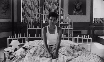 Movie still from “She's Gotta Have It” (1986), directed by Spike Lee – A black and white photo of a woman sitting on a bed; Medium shot, High angle