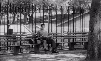Movie still from “She's Gotta Have It” (1986), directed by Spike Lee – A man sitting on top of a wooden bench; Wide shot, Low angle