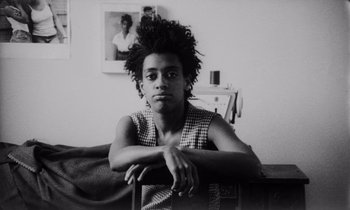 Movie still from “She's Gotta Have It” (1986), directed by Spike Lee – A black and white photo of a man sitting on a couch; Close Up shot, Low angle