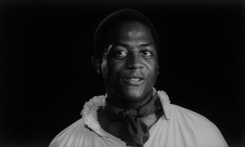 Movie still from “She's Gotta Have It” (1986), directed by Spike Lee – A black and white photo of a man in a white shirt and a neck tie; Close Up shot, Low angle