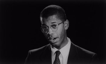 Movie still from “She's Gotta Have It” (1986), directed by Spike Lee – A black and white photo of a man in a suit and tie; Close Up shot, Low angle