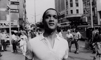 Movie still from “She's Gotta Have It” (1986), directed by Spike Lee – Black and white photograph of a man standing in front of a group of people; Close Up shot, Low angle