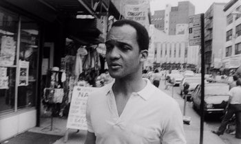 Movie still from “She's Gotta Have It” (1986), directed by Spike Lee – A black and white photo of a man standing in the middle of a street; Close Up shot, Low angle