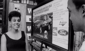 Movie still from “She's Gotta Have It” (1986), directed by Spike Lee – A woman standing in front of an advertisement; Medium shot, Over the shoulder angle