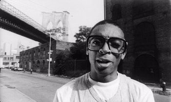Movie still from “She's Gotta Have It” (1986), directed by Spike Lee – A black and white photo of a man wearing glasses; Close Up shot, Low angle