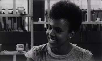 Movie still from “She's Gotta Have It” (1986), directed by Spike Lee – A black and white photo of a woman smiling; Close Up shot, Over the shoulder angle