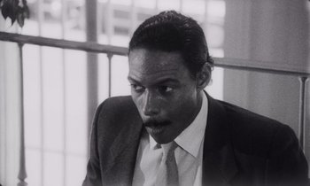 Movie still from “She's Gotta Have It” (1986), directed by Spike Lee – A black and white photo of a man in a suit and tie; Close Up shot, High angle