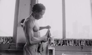 Movie still from “She's Gotta Have It” (1986), directed by Spike Lee – A shirtless man is holding a pair of pants; Medium shot, Low angle