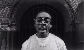 Movie still from “She's Gotta Have It” (1986), directed by Spike Lee – Black and white photograph of a man with glasses; Close Up shot, Low angle