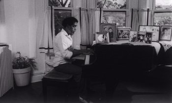 Movie still from “She's Gotta Have It” (1986), directed by Spike Lee – A man sitting at a piano in front of a window; Medium shot, High angle