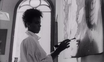 Movie still from “She's Gotta Have It” (1986), directed by Spike Lee – A black and white photo of a woman painting a picture; Medium shot, Low angle