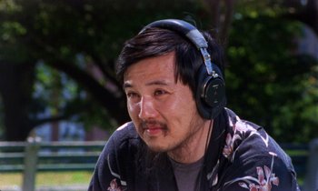 Movie still from “She's Gotta Have It” (1986), directed by Spike Lee – A man with headphones sitting in a park; Close Up shot, High angle