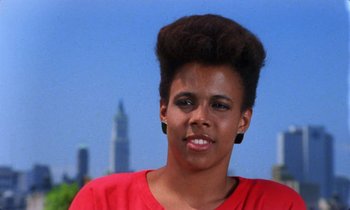 Movie still from “She's Gotta Have It” (1986), directed by Spike Lee – A young woman with a large hair style in front of a city skyline; Close Up shot, Low angle