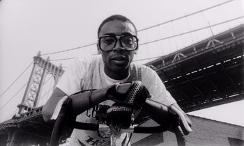 Movie still from “She's Gotta Have It” (1986), directed by Spike Lee – A black and white photo of a man wearing glasses; Close Up shot, Low angle