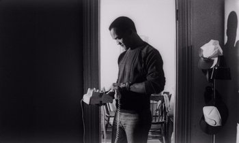 Movie still from “She's Gotta Have It” (1986), directed by Spike Lee – A black and white photo of a man holding a phone; Medium shot, Low angle