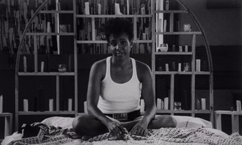 Movie still from “She's Gotta Have It” (1986), directed by Spike Lee – A black and white photo of a woman sitting on the floor; Medium shot, Low angle
