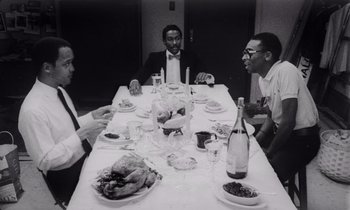 Movie still from “She's Gotta Have It” (1986), directed by Spike Lee – A black and white photo of people sitting at a dinner table; Medium shot, High angle
