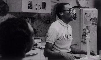 Movie still from “She's Gotta Have It” (1986), directed by Spike Lee – An old black and white photo of a man in a kitchen; Close Up shot, Over the shoulder angle