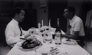 Movie still from “She's Gotta Have It” (1986), directed by Spike Lee – A black and white photo of two men sitting at a dinner table; Medium shot, High angle