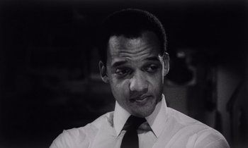 Movie still from “She's Gotta Have It” (1986), directed by Spike Lee – Black and white photograph of a man in a white dress shirt and tie; Close Up shot, Low angle