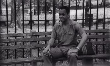 Movie still from “She's Gotta Have It” (1986), directed by Spike Lee – A black and white photo of a man sitting on a bench; Medium shot, High angle