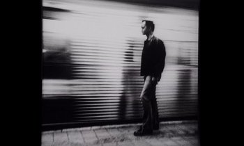 Movie still from “She's Gotta Have It” (1986), directed by Spike Lee – A black and white photo of a man standing on the side of the street; Wide shot, Low angle