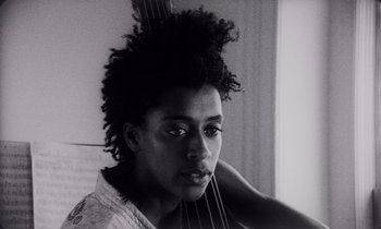Movie still from “She's Gotta Have It” (1986), directed by Spike Lee – A black and white photo of a woman holding a cello; Close Up shot, Low angle