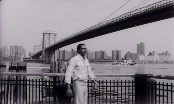 Movie still from “She's Gotta Have It” (1986), directed by Spike Lee – A black and white photo of a man standing in front of a bridge; Wide shot, Low angle