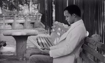 Movie still from “She's Gotta Have It” (1986), directed by Spike Lee – A black and white photo of a man sitting on a park bench; Medium shot, Low angle