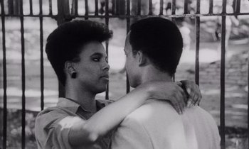 Movie still from “She's Gotta Have It” (1986), directed by Spike Lee – A couple of men standing next to each other near a fence; Close Up shot, Low angle