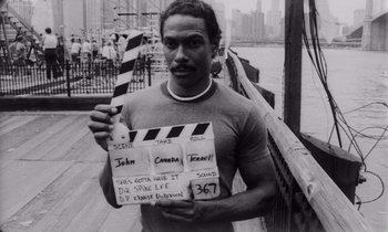 Movie still from “She's Gotta Have It” (1986), directed by Spike Lee – A black and white photo of a man holding a clapperboard; Close Up shot, High angle