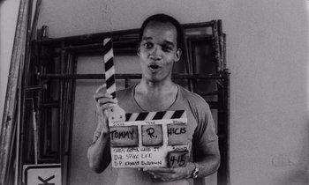 Movie still from “She's Gotta Have It” (1986), directed by Spike Lee – A black and white photo of a man holding a clapperboard; Close Up shot, High angle