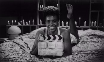 Movie still from “She's Gotta Have It” (1986), directed by Spike Lee – A black and white photo of a woman holding a clapperboard; Medium shot, Low angle