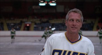 Movie still from “Slap Shot” (1977), directed by George Roy Hill – A man in a white and blue hockey uniform; Medium shot, Low angle