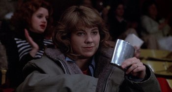 Movie still from “Slap Shot” (1977), directed by George Roy Hill – A young woman holding a metal object while sitting in a crowd; Close Up shot, Low angle