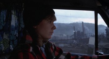Movie still from “Slap Shot” (1977), directed by George Roy Hill – A person sitting in a car looking out the window; Medium shot, High angle