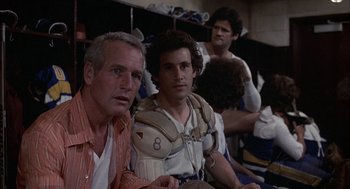 Movie still from “Slap Shot” (1977), directed by George Roy Hill – A group of men sitting next to each other in a room; Close Up shot, Low angle